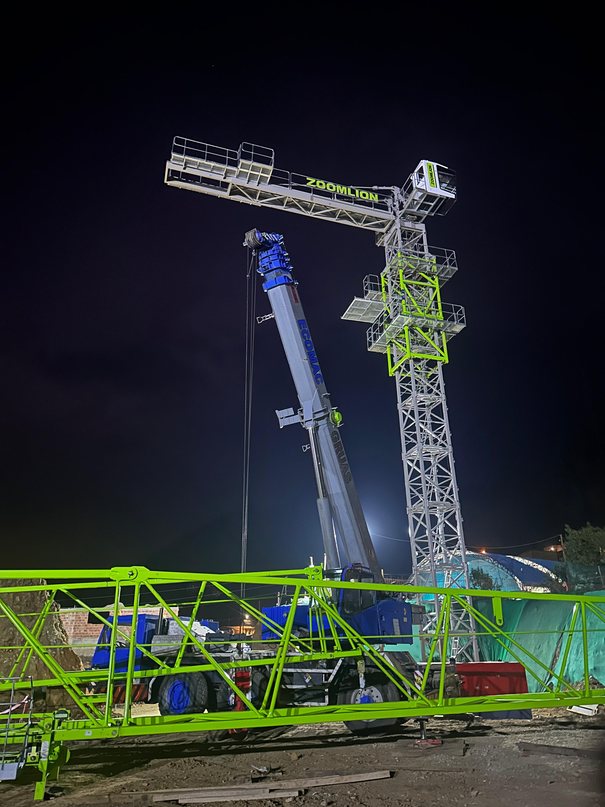 Grúa torre iluminada de noche durante su montaje con una grúa telescópica